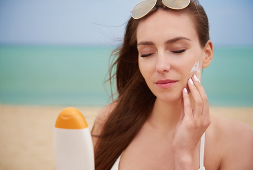 The women is applying sunscreen on her face and providing extra care for her sensitive skin